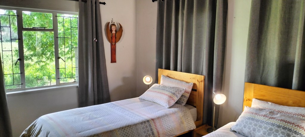 Cozy twin bedroom in a guesthouse with wooden furniture, patterned bedding, and a window showcasing natural greenery outside.