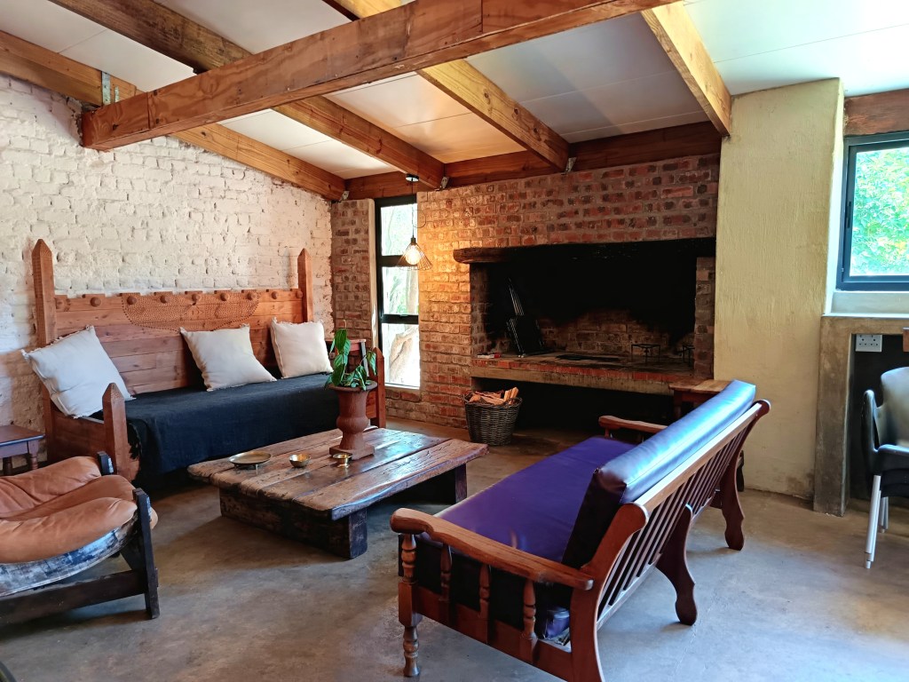 Cozy interior of a guesthouse featuring wooden beams, rustic furniture, a fireplace, and large windows inviting natural light.