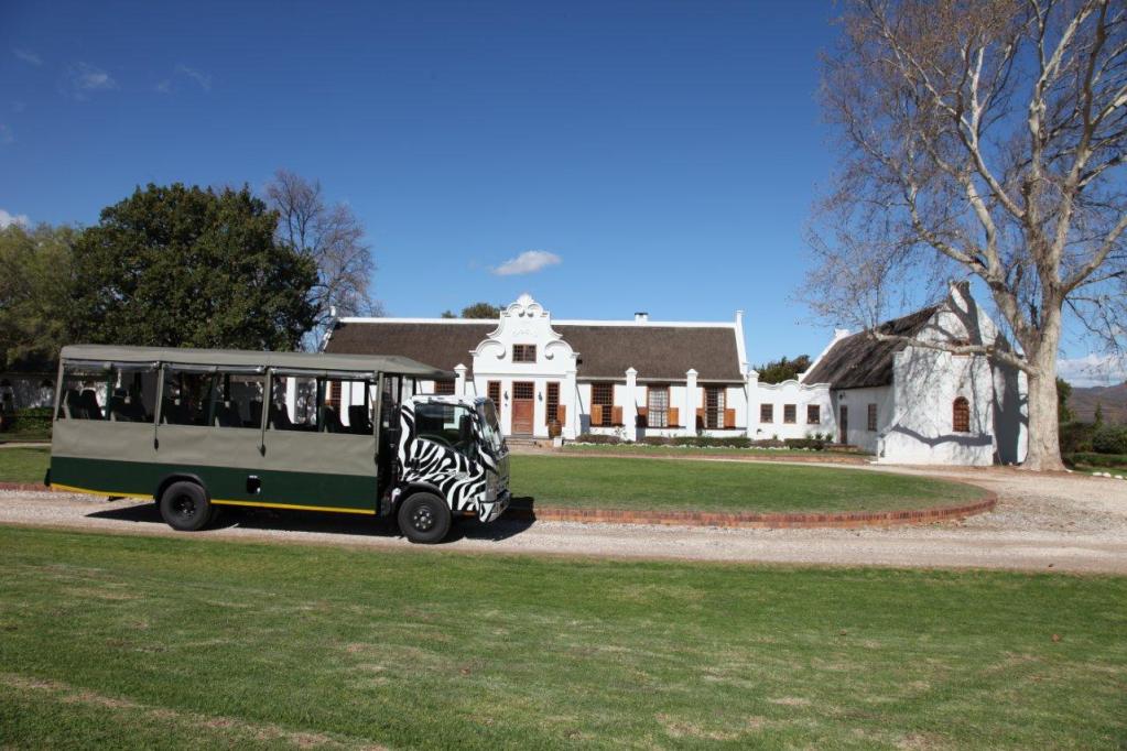 A zebra-striped safari vehicle parked in front of a historic white building surrounded by greenery under a clear blue sky.