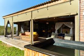 A stylish outdoor view of a modern tented accommodation featuring a spacious deck, furniture, and a hot tub.