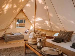 Interior of a stylish, spacious tent featuring two beds with cushions, a rustic wooden table with decorative pottery, and a warm, inviting atmosphere.
